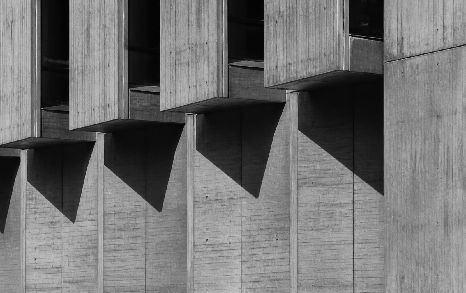 Repeating raw concrete facade panels casting hard geometric shadows